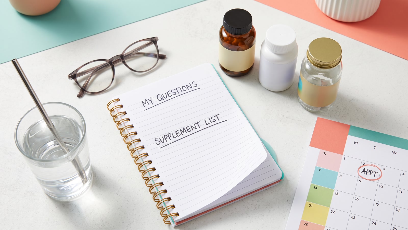Notebook, calendar, and supplement bottles arranged for a routine planning session.